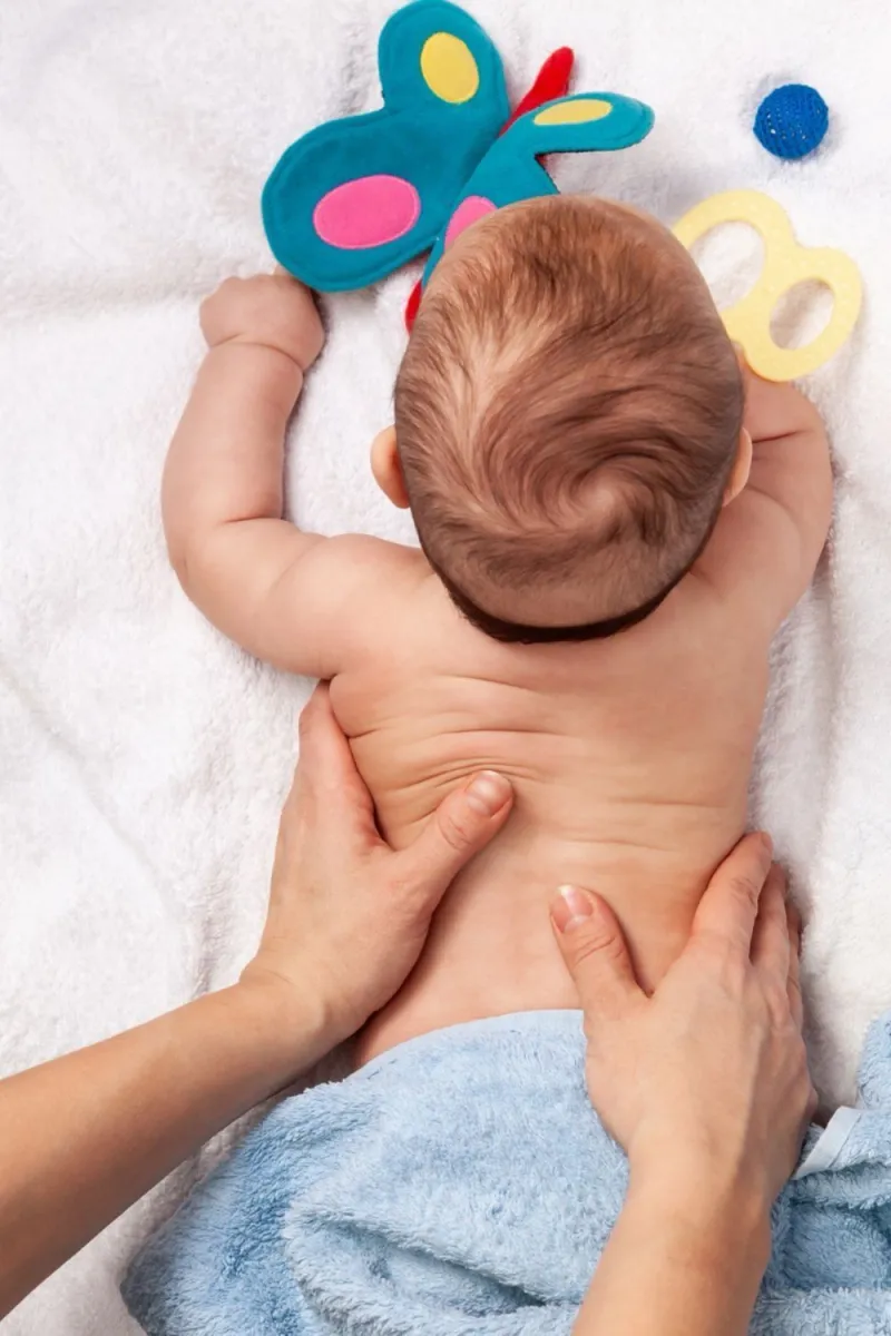 Baby wird sanft am Rücken massiert, daneben ein Schmetterlings-Spielzeug