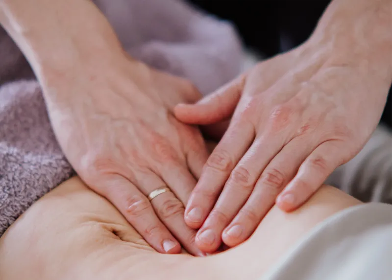 Hände liegen sanft übereinander auf dem Bauch einer Patientin während der viszeralen Behandlung